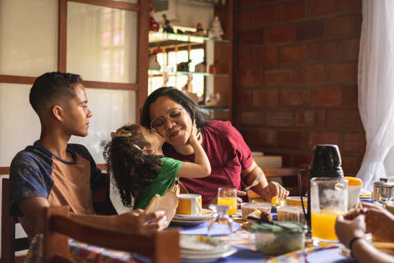 Family at breakfast table, little girl hugging Mom