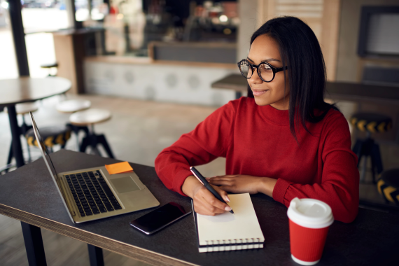 Reporter with pen, pad, laptop, phone, coffee on her desk