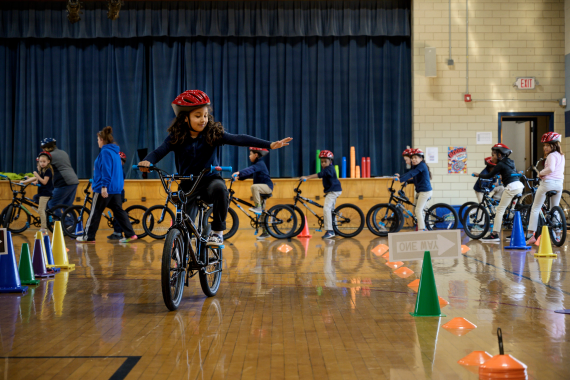 Young girl riding a bike through obstacle course in a gym