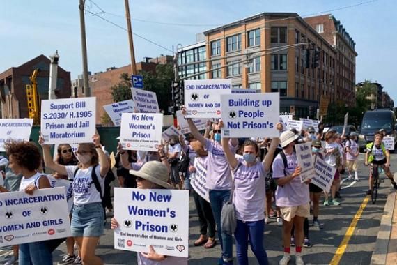 Protesters in street hold signs, No New Women's Prison