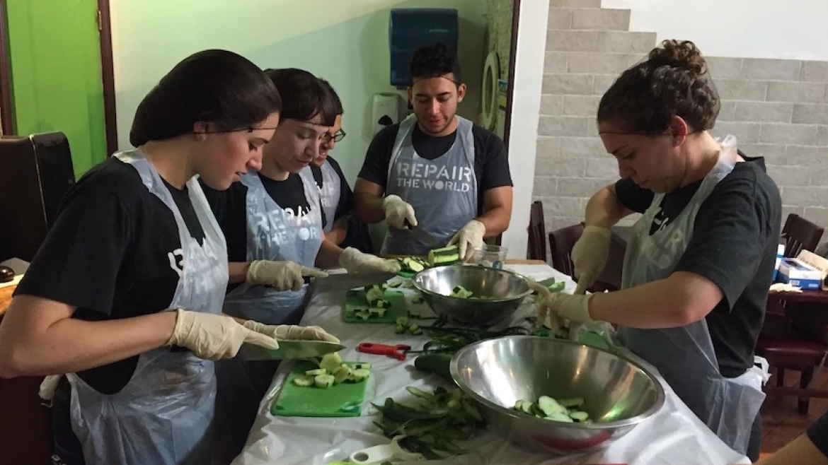 Five volunteers for Repair the World in aprons preparing cucumber salad for a group