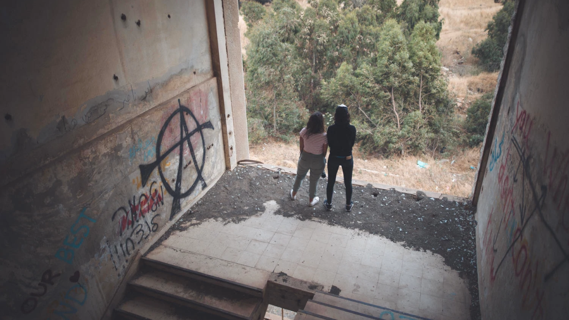 Two people, abandoned building with graffiti, open wall view of outside