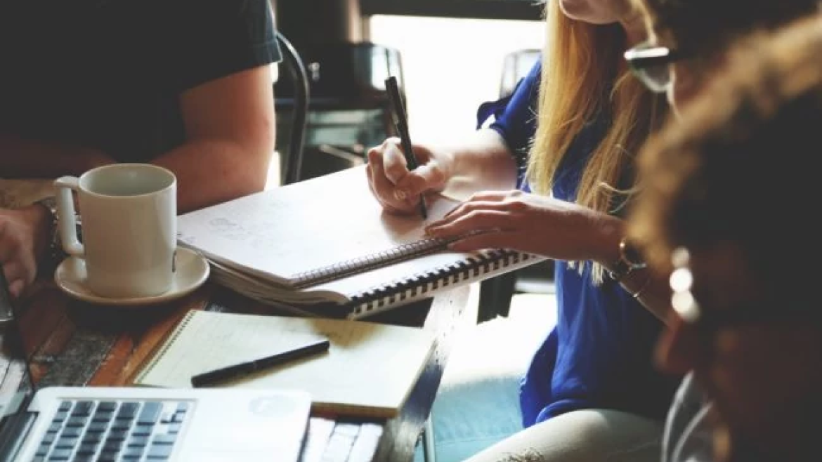 Small group around a table with notebook, pens, laptop, coffee