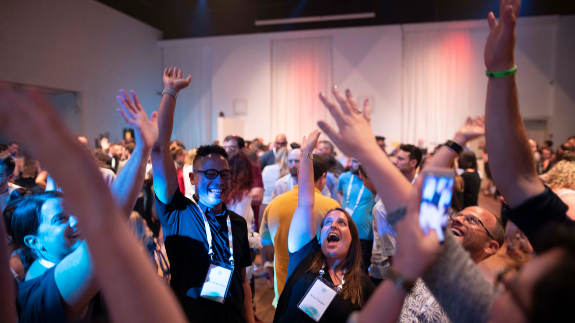 As part of a larger crowd, a small circle of people, stretching arms up, having fun in a group activity