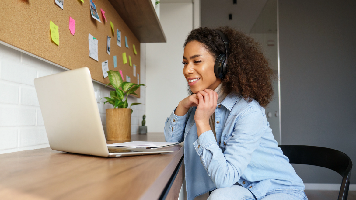 Woman with headphones, smiling, watching her laptop screen