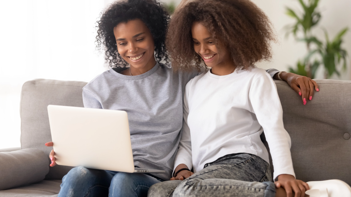 Two young women on couch smile and share a laptop screen