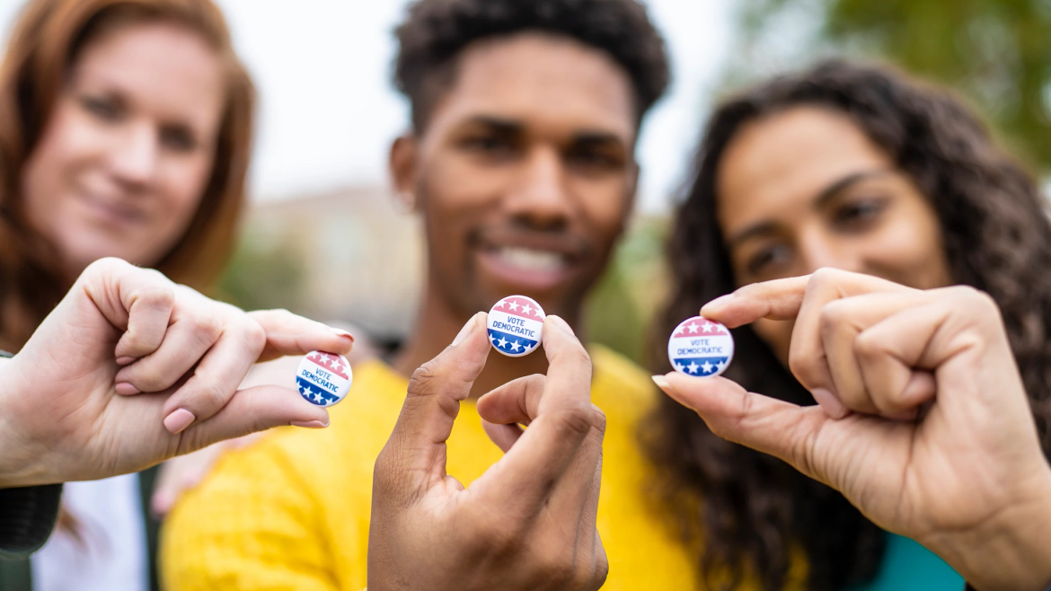 Young voters holding up buttons that read, "Vote Democratic".