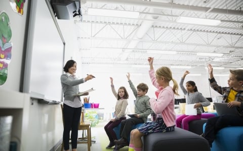 teacher pointing to students with hands raised - Instruction Partners